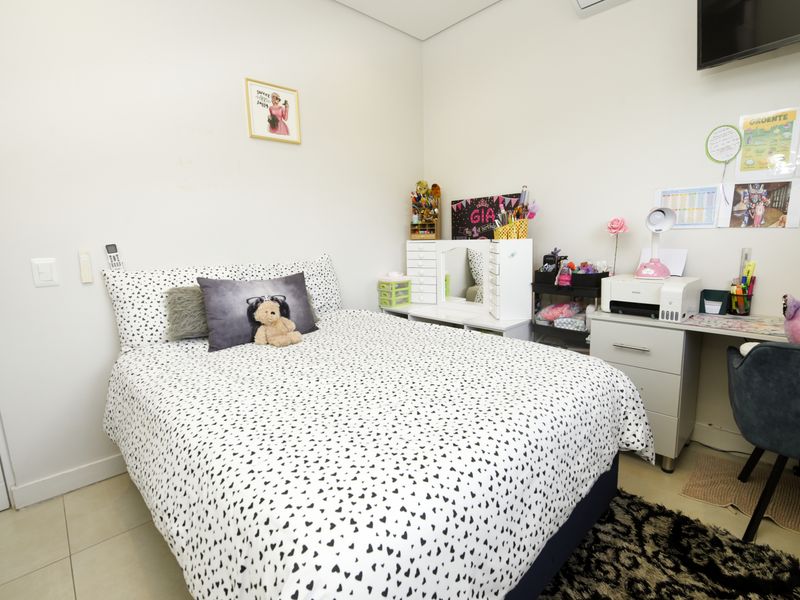 A well-maintained bedroom featuring tiled flooring, a built-in desk area, and an integrated air conditioning unit.