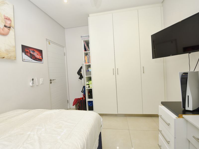 A well-maintained bedroom featuring neutral tiled flooring, built-in floor-to-ceiling cupboards, and clean white finishes, providing a bright and functional living space.