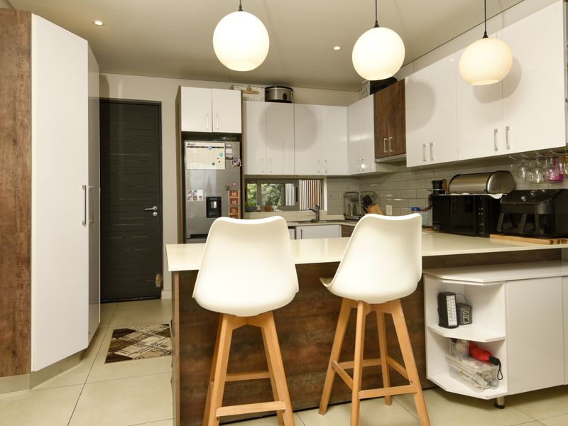 Modern kitchen featuring white and wood-tone cabinetry, stone countertops, subway tile backsplash, and stylish pendant lighting with a functional breakfast bar area.