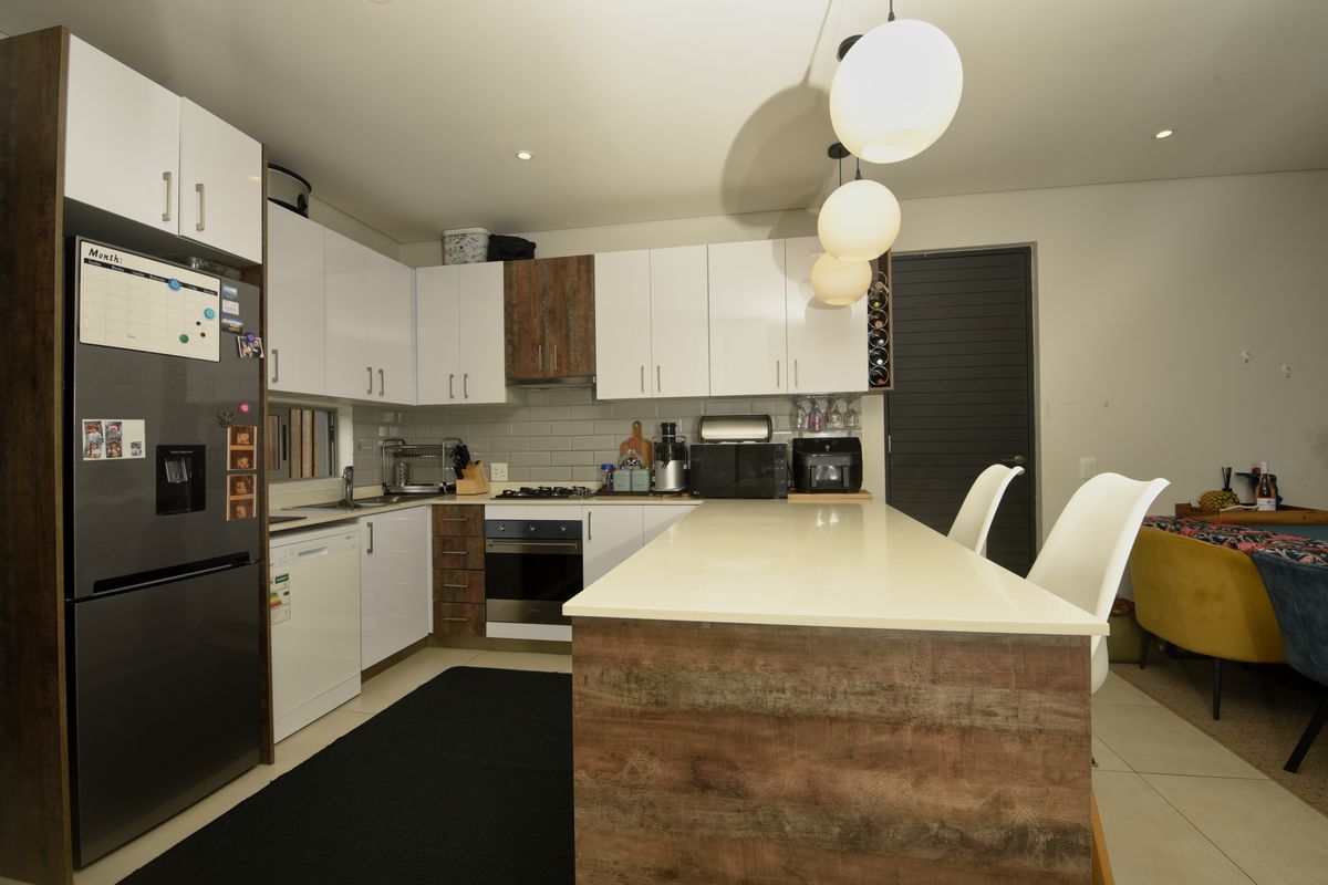 Modern kitchen featuring high-gloss cabinetry, a central island with stone countertop, subway tile backsplash, and integrated appliances, flowing into an open-plan living area.