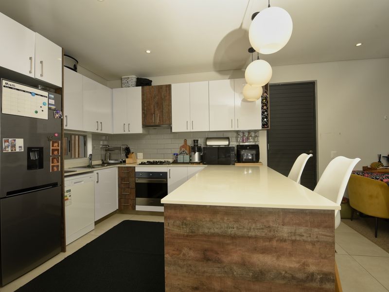 Modern kitchen featuring high-gloss cabinetry, a central island with stone countertop, subway tile backsplash, and integrated appliances, flowing into an open-plan living area.