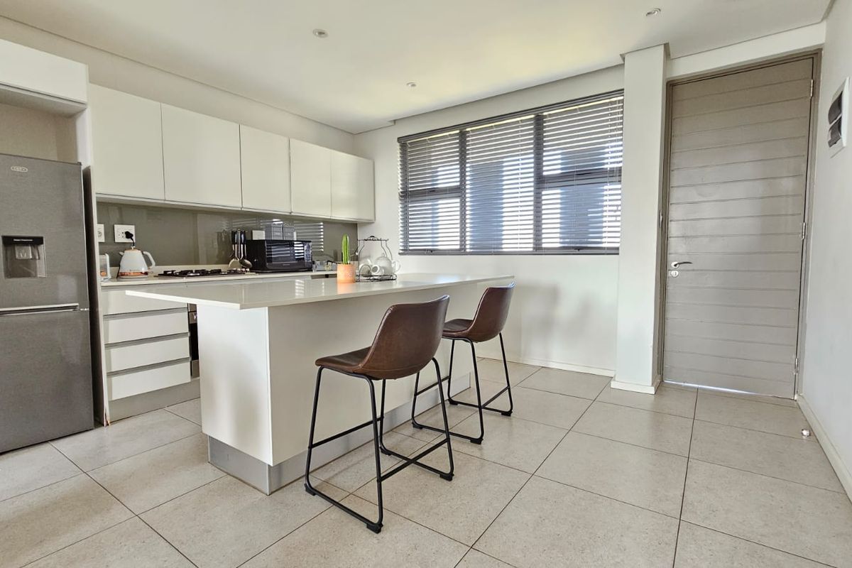 Modern kitchen featuring white cabinetry, a central island with stone countertops, gas hob, and tiled flooring, offering a clean and functional workspace.