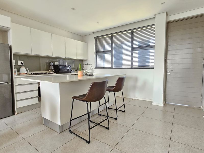 Modern kitchen featuring white cabinetry, a central island with stone countertops, gas hob, and tiled flooring, offering a clean and functional workspace.