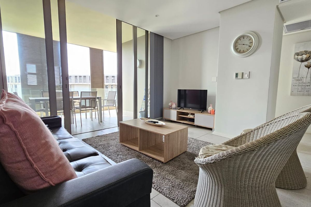 A bright, modern living room featuring tiled floors, recessed lighting, and large sliding glass doors that open onto a private balcony.
