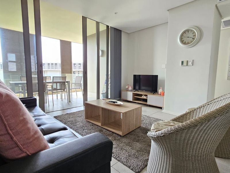 A bright, modern living room featuring tiled floors, recessed lighting, and large sliding glass doors that open onto a private balcony.