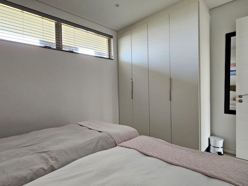 A modern bedroom featuring built-in cupboards, a horizontal window with venetian blinds, and recessed downlighting.