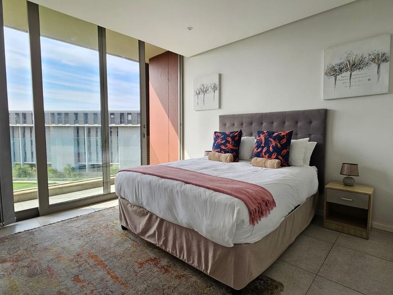 A bright, modern bedroom featuring large floor-to-ceiling sliding glass doors that provide ample natural light and access to an outdoor area.