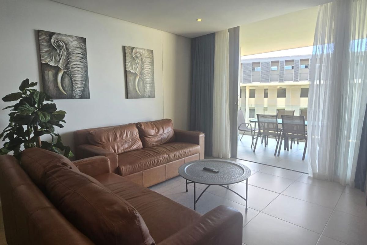 A bright living room featuring tiled flooring and large sliding glass doors that open onto a private balcony.