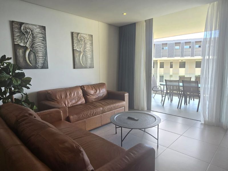A bright living room featuring tiled flooring and large sliding glass doors that open onto a private balcony.
