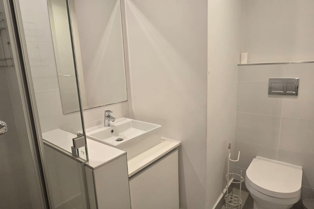 Modern bathroom featuring a wall-hung toilet with concealed cistern, a vessel sink vanity, and a glass-enclosed shower with tiled finishes.