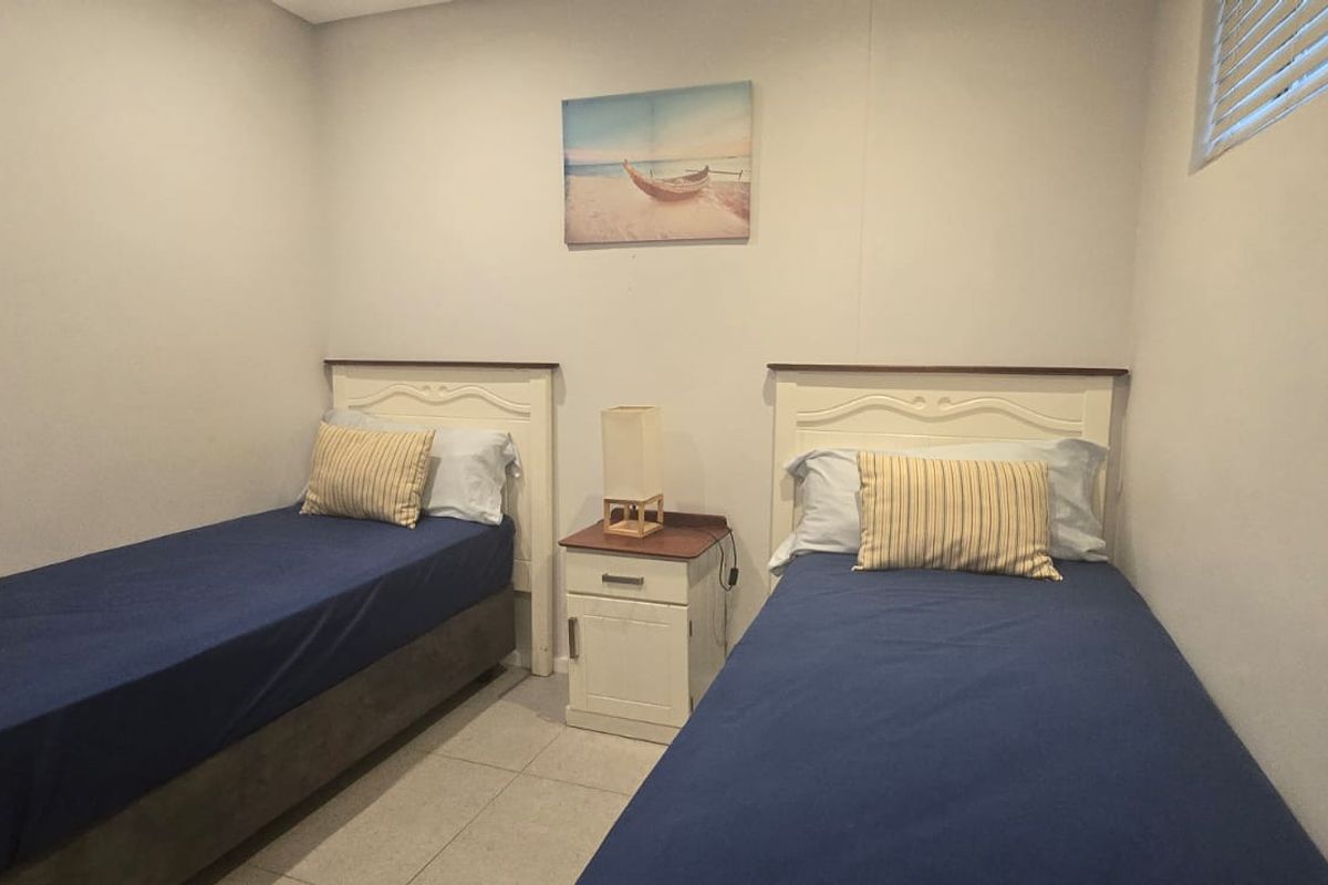 A functional bedroom featuring tiled flooring and window blinds, currently configured with twin beds.
