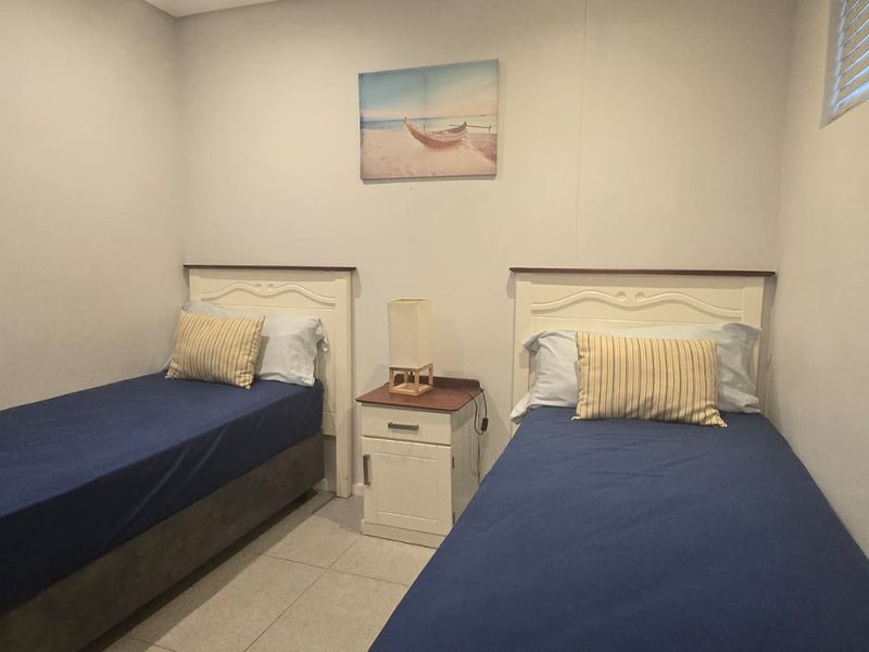 A functional bedroom featuring tiled flooring and window blinds, currently configured with twin beds.