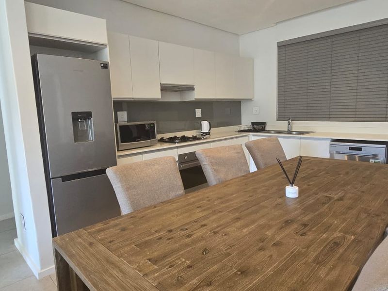 Modern open-plan kitchen and dining area featuring sleek white cabinetry, integrated appliances, gas hob, and neutral tiled flooring.