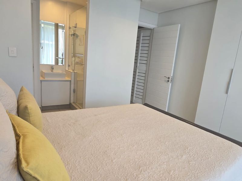 Modern bedroom featuring built-in cupboards and a compact en-suite bathroom with a glass shower enclosure and vanity basin.