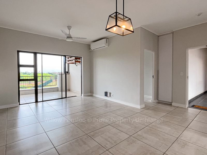 Spacious, light-filled living area featuring neutral tiled flooring, a ceiling fan, air conditioning, and direct access to a private balcony.