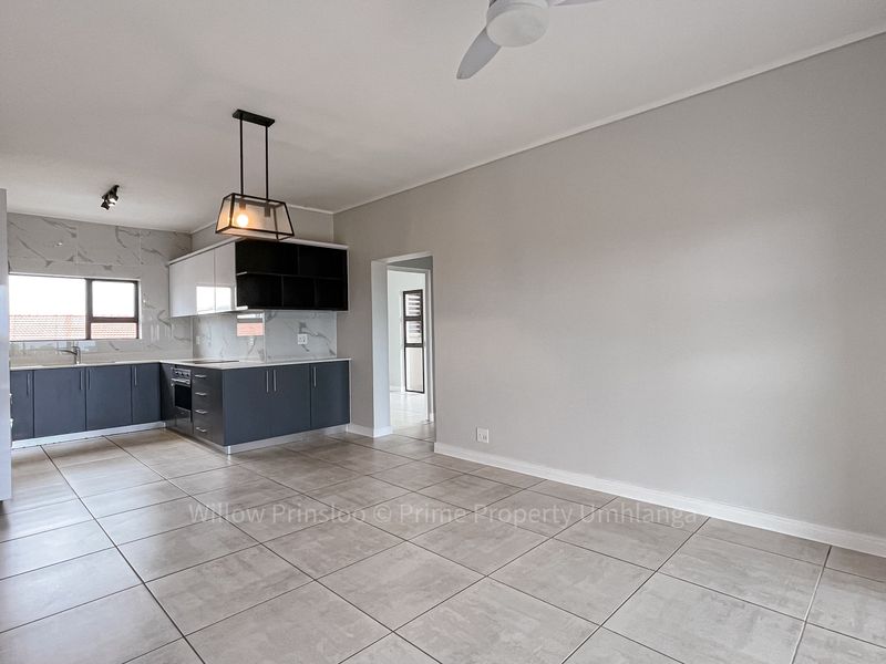 Modern open-plan kitchen and living area featuring sleek dark cabinetry, marble-look splashbacks, and neutral tiled flooring throughout.