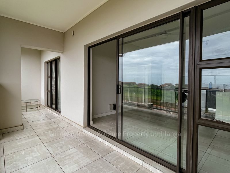 A spacious covered balcony featuring tiled flooring, large sliding glass doors, and a metal balustrade, offering a clean and functional outdoor living space.