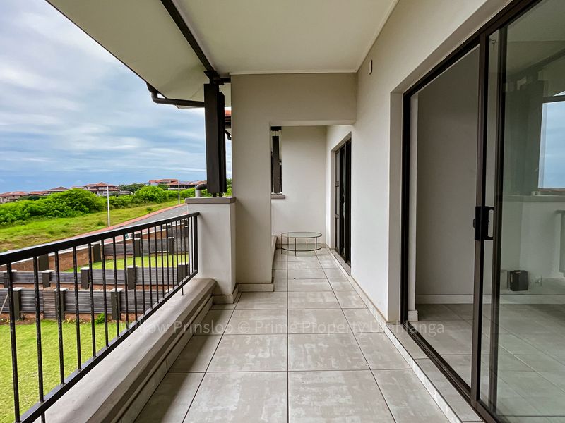 A spacious covered balcony featuring tiled flooring, a metal balustrade, and large sliding glass doors providing access to the interior living space.