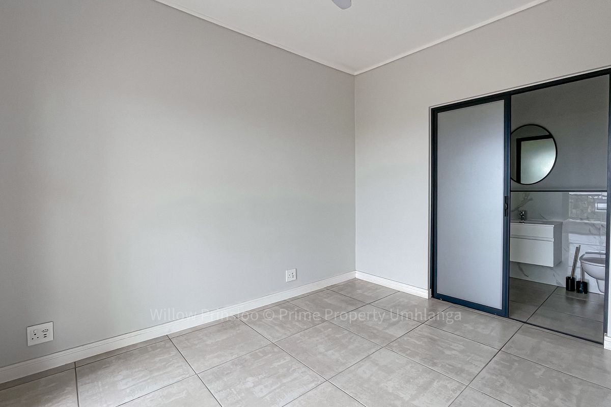 A clean, empty bedroom featuring neutral tiled flooring, modern skirting boards, and a sliding door leading to an en-suite bathroom.