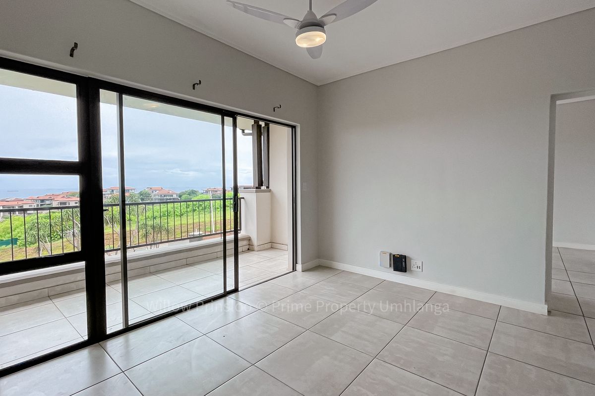 Bright and spacious living area featuring neutral tiled flooring, a ceiling fan, and large sliding glass doors leading to a private balcony.