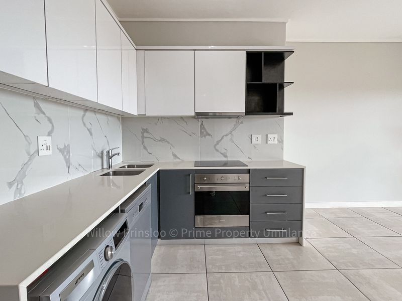 Modern kitchen featuring sleek white and grey cabinetry, stone countertops, marble-look splashback, and integrated stainless steel appliances.