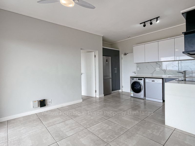 Modern open-plan kitchen and living area featuring sleek white cabinetry, marble-look backsplash, tiled flooring, and integrated lighting in a clean, contemporary apartment setting.