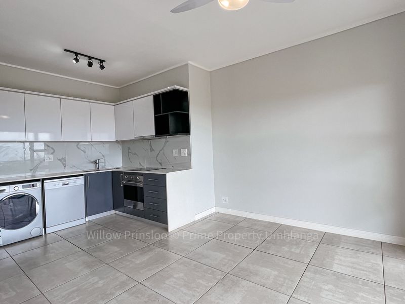 Modern open-plan kitchen featuring sleek white and grey cabinetry, marble-look splashbacks, integrated appliances, and neutral tiled flooring in a bright, spacious layout.