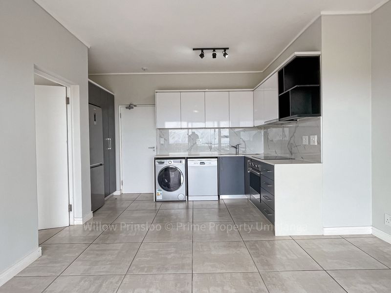 Modern kitchen featuring sleek two-tone cabinetry, stone countertops, integrated appliances, and neutral tiled flooring in an open-plan layout.