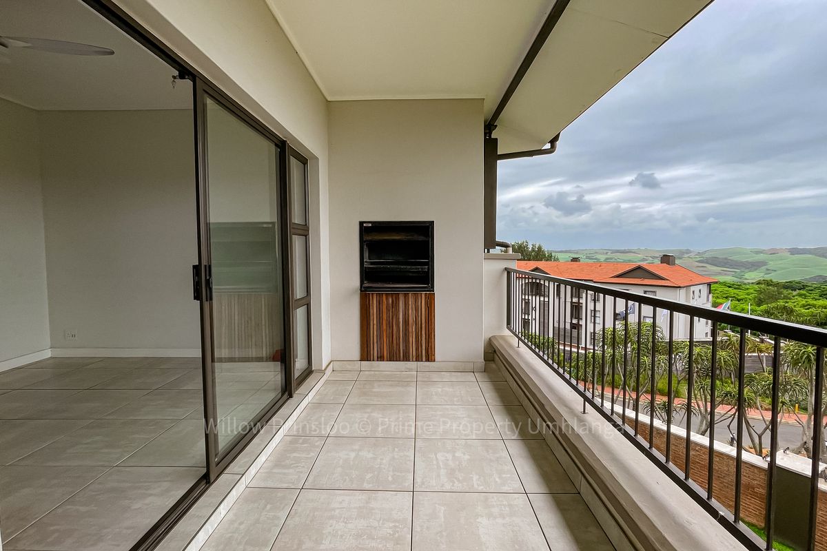 Spacious covered balcony featuring tiled flooring, a built-in braai, and sliding door access, offering scenic views of the surrounding landscape.