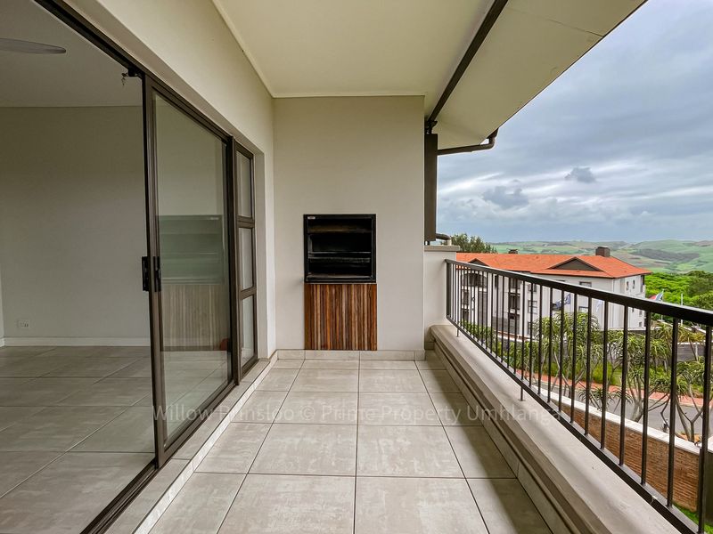 Spacious covered balcony featuring tiled flooring, a built-in braai, and sliding door access, offering scenic views of the surrounding landscape.