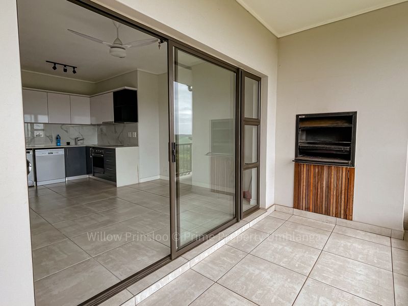 Covered balcony featuring a built-in braai, tiled flooring, and seamless access to an open-plan kitchen area with modern cabinetry.