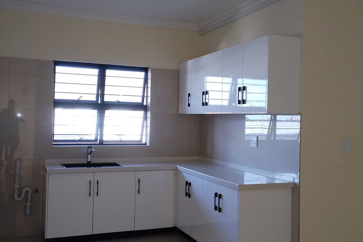 A clean, modern kitchen featuring white gloss cabinetry, a dark sink, tiled splashbacks, and ample countertop space in an empty, well-maintained apartment setting.