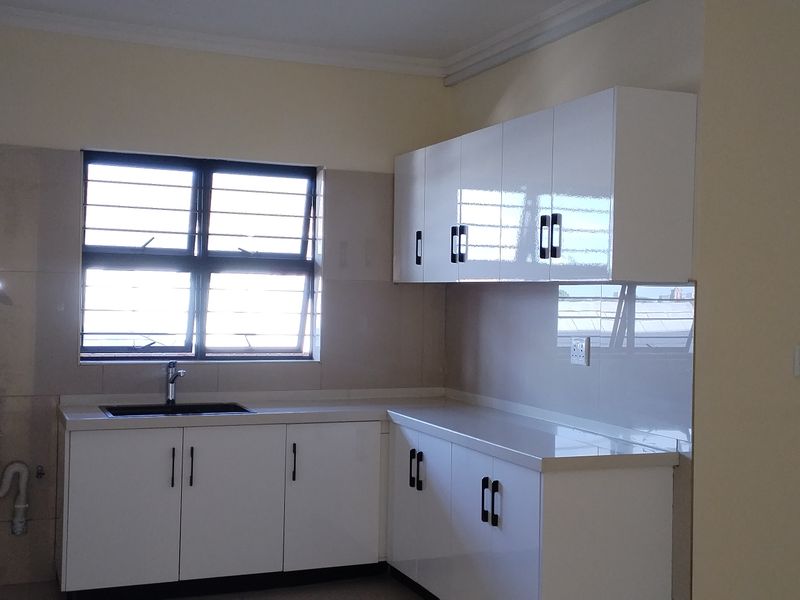 A clean, modern kitchen featuring white gloss cabinetry, a dark sink, tiled splashbacks, and ample countertop space in an empty, well-maintained apartment setting.