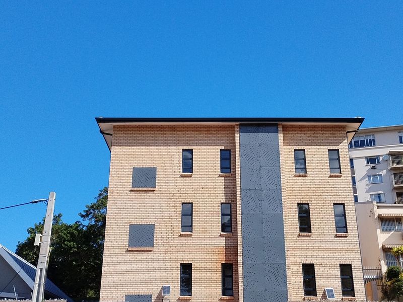 A view of the front facade of a multi-story brick apartment building featuring modern metal cladding accents and standard window configurations.