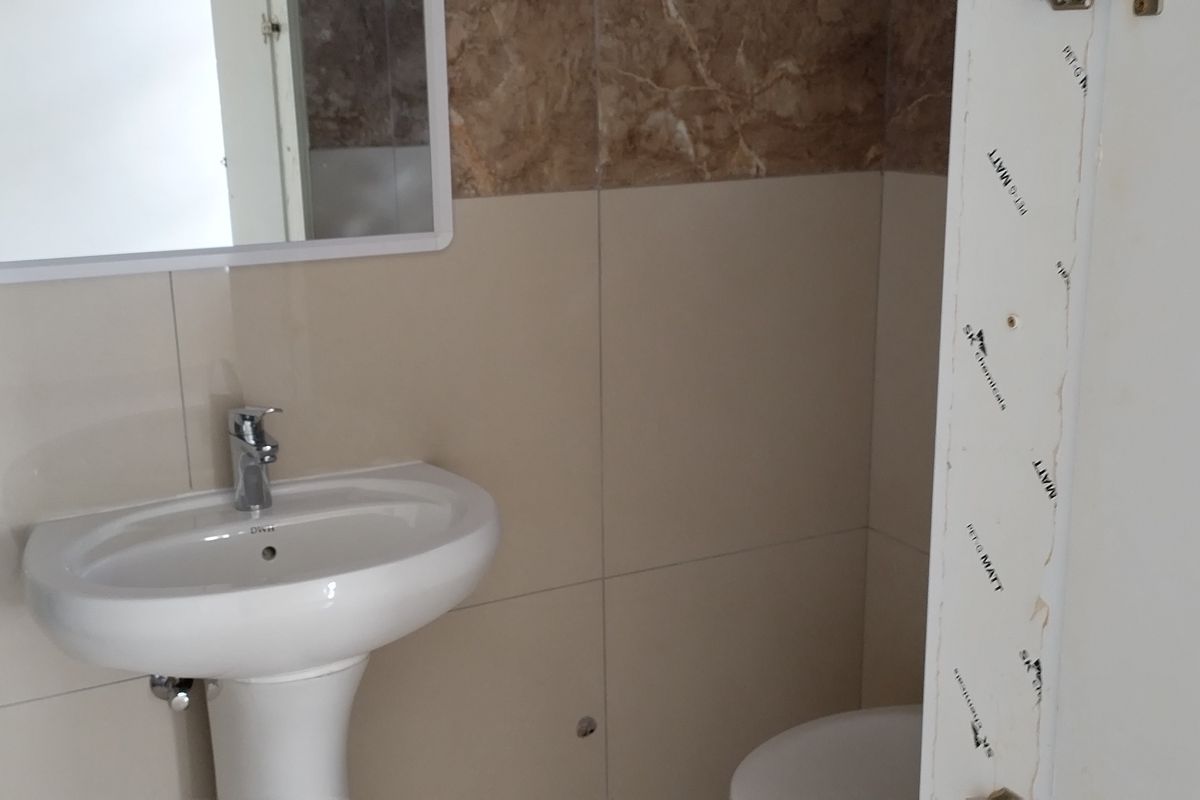 A modern bathroom featuring a pedestal basin, chrome fixtures, and neutral wall tiling, currently awaiting final finishing touches.