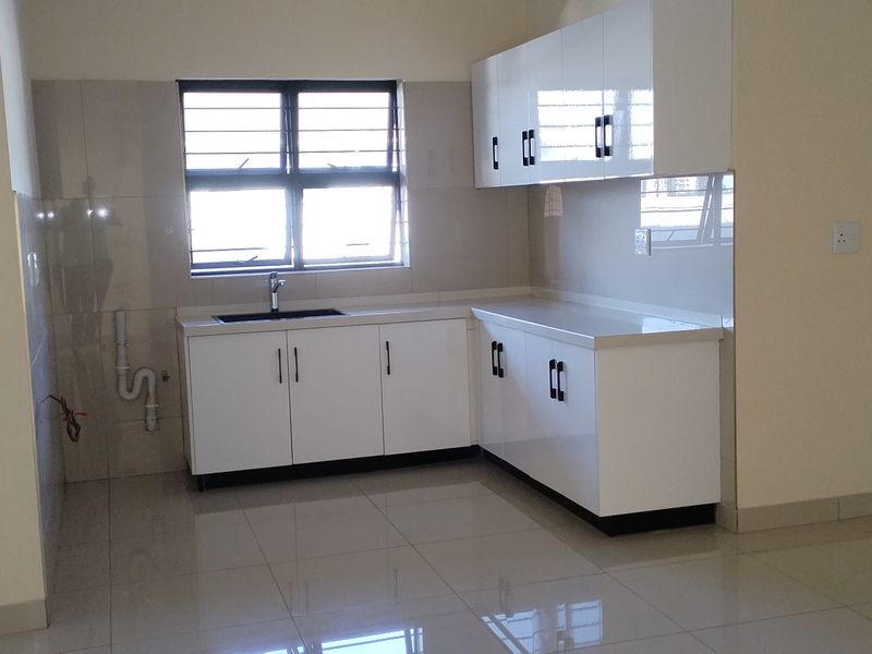 A clean, modern kitchen featuring white high-gloss cabinetry, tiled flooring, and a functional sink area with a tiled backsplash.