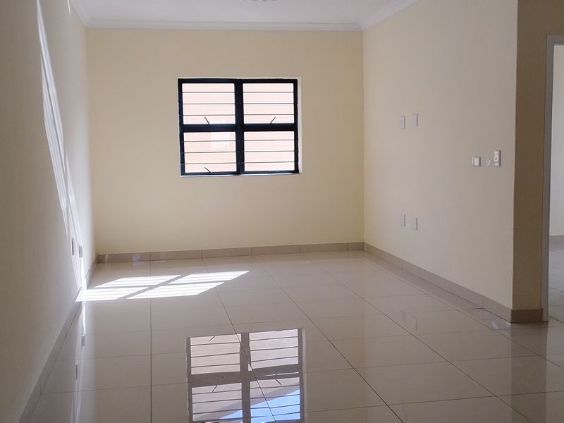 A bright, empty living area featuring neutral walls, polished tiled flooring, and a window fitted with security bars.