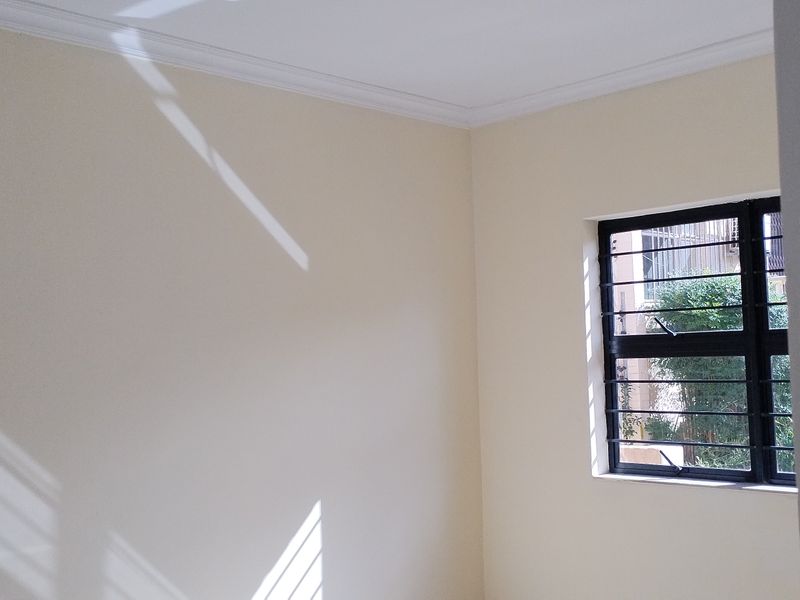 A bright, empty bedroom featuring neutral walls, crown molding, and a window fitted with security bars.