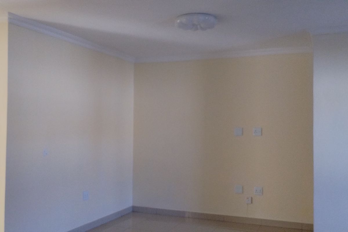 A bright, empty living area featuring neutral walls, tiled flooring, and ceiling cornice detailing, providing a clean canvas for interior design.