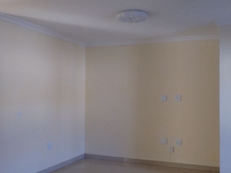 A bright, empty living area featuring neutral walls, tiled flooring, and ceiling cornice detailing, providing a clean canvas for interior design.