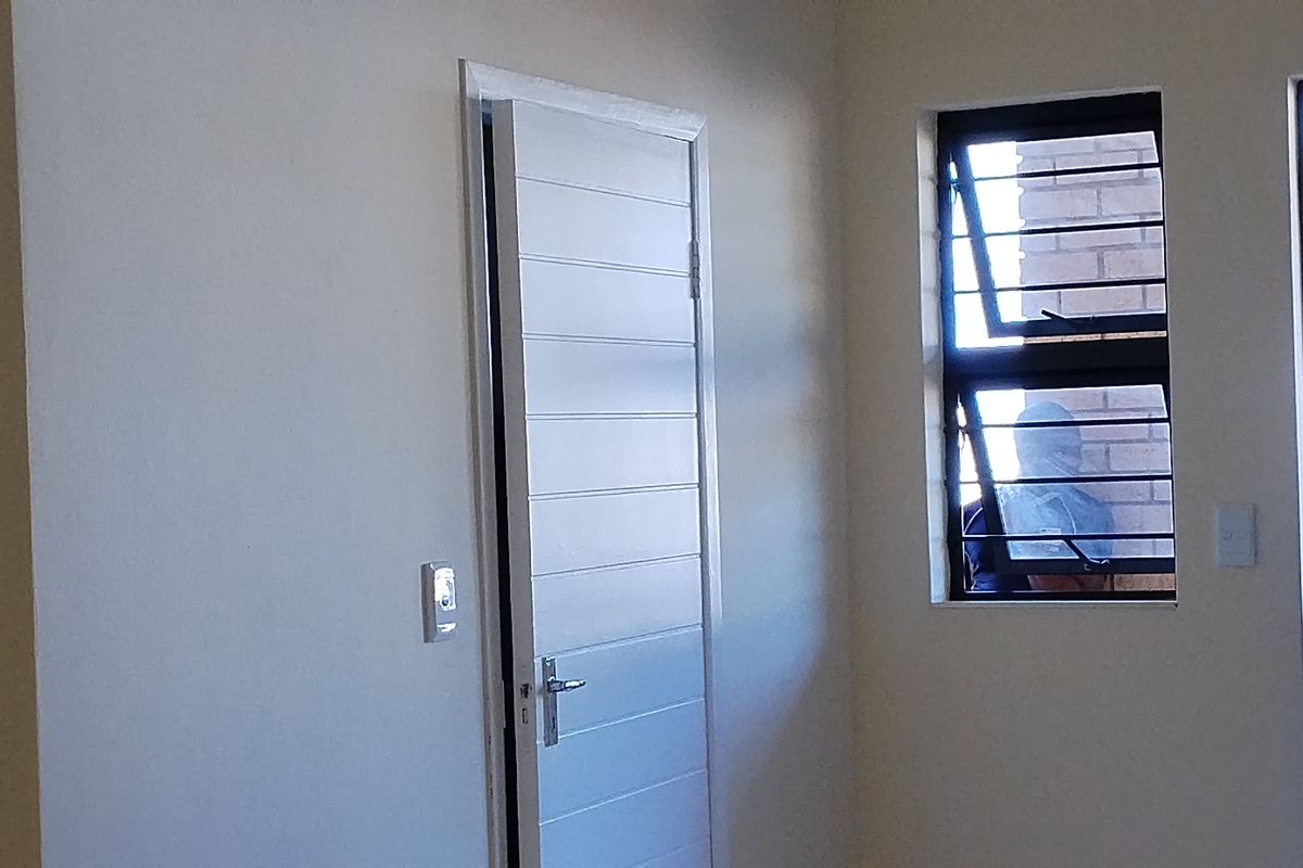 A clean, empty bedroom featuring a horizontal panel door, casement window with security bars, and neutral wall finishes.