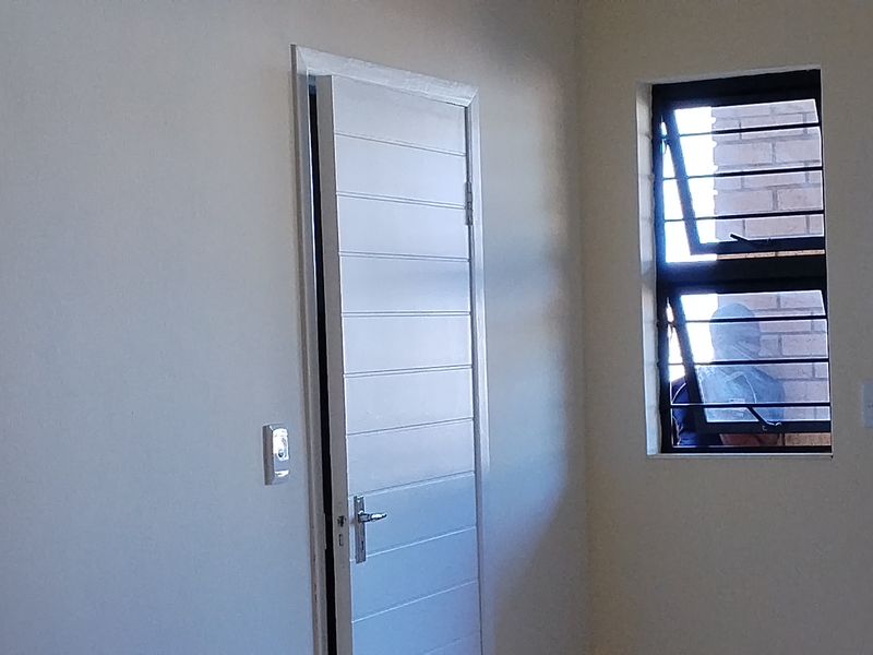 A clean, empty bedroom featuring a horizontal panel door, casement window with security bars, and neutral wall finishes.