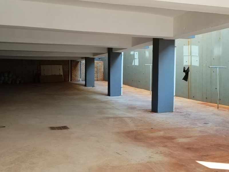 A large, open-plan basement garage area featuring concrete flooring, structural columns, and exposed brick and retaining walls.
