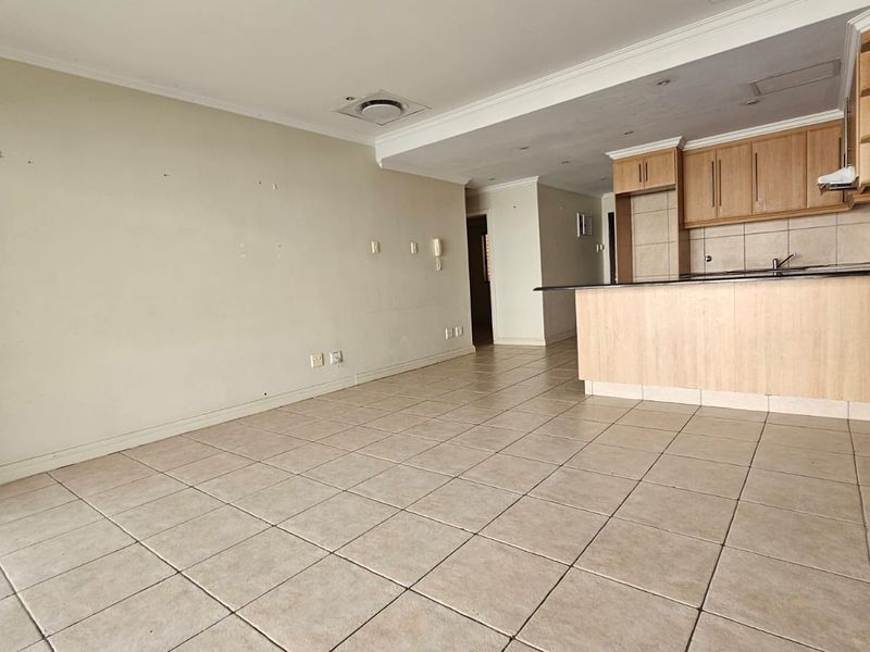 An open-plan living and kitchen area featuring tiled flooring, wooden cabinetry, and a granite breakfast bar, offering a blank canvas for personalization.