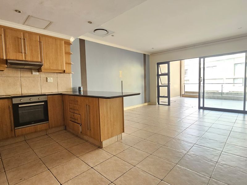 Spacious open-plan kitchen and living area featuring wooden cabinetry, granite countertops, tiled flooring, and large sliding doors leading to a balcony.