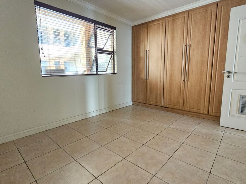 An empty bedroom featuring tiled flooring, built-in wooden cupboards, and a window with venetian blinds.