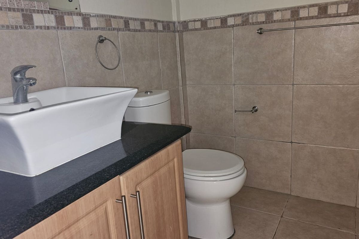 A functional bathroom featuring a vessel sink on a vanity cabinet, tiled walls with a decorative border, and a standard toilet.