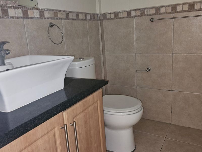 A functional bathroom featuring a vessel sink on a vanity cabinet, tiled walls with a decorative border, and a standard toilet.