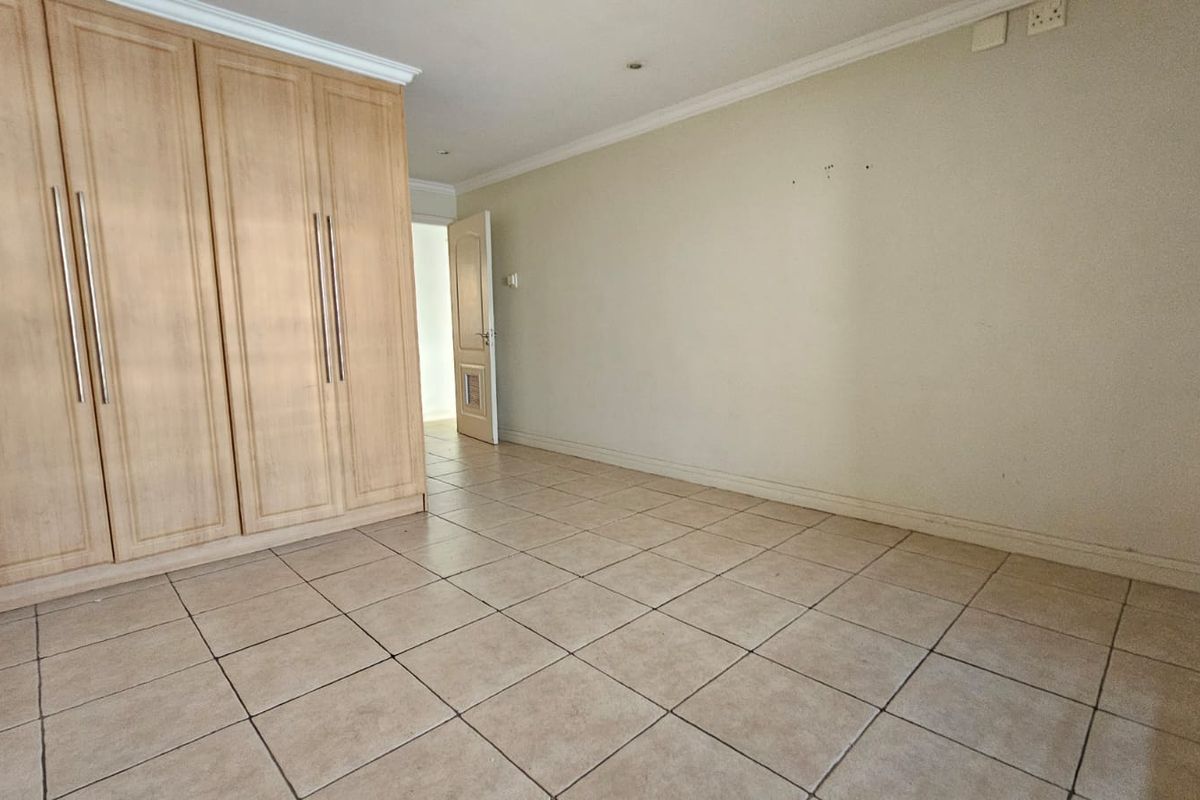 An empty bedroom featuring tiled flooring, coved cornicing, and built-in wooden cupboards, offering a neutral space ready for personalization.