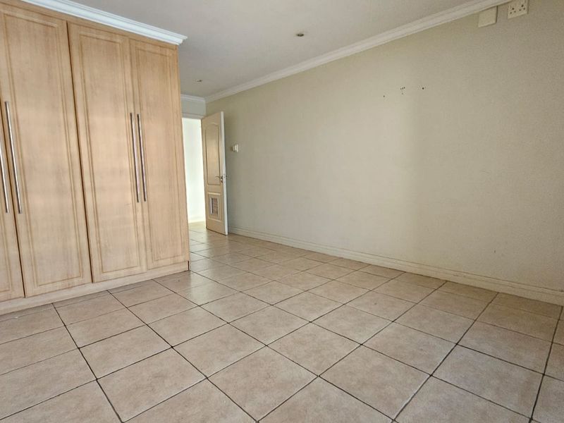 An empty bedroom featuring tiled flooring, coved cornicing, and built-in wooden cupboards, offering a neutral space ready for personalization.